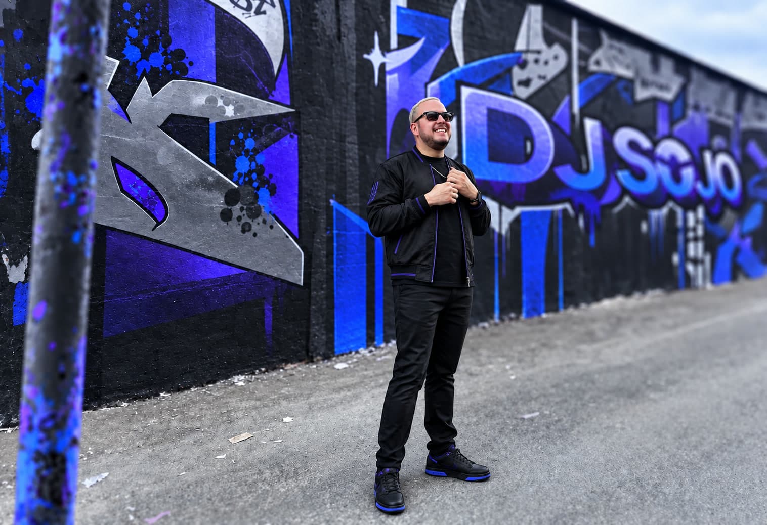 DJ Sojo in front of his blue and violet street-art mural